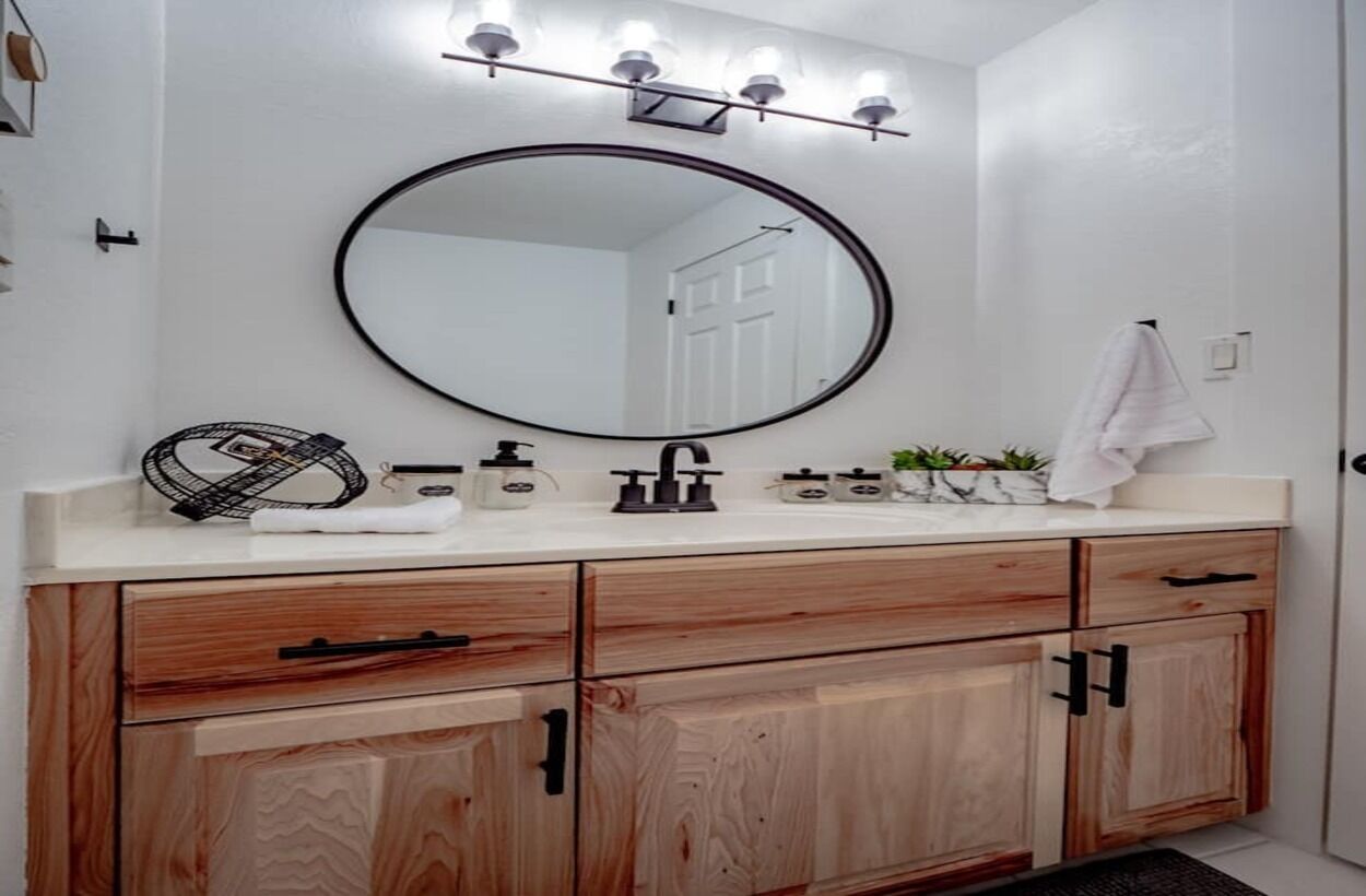 A bathroom with a wooden vanity, a round mirror with lights, and a towel hanging on the wall.