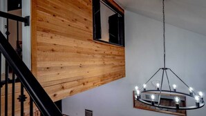 Un intérieur moderne avec un plafond en pente en bois, un escalier noir et un lustre à plusieurs ampoules.
