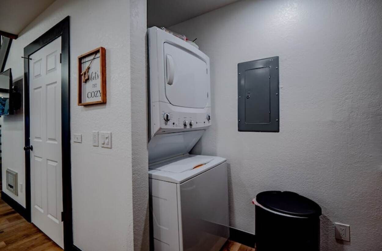 Un lavadero con lavadora y secadora, un cubo de basura y un termostato en la pared.