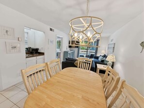 A dining area with a wooden table and chairs, a hanging light fixture, and a kitchen in the background. - Renovated Beach Villa 14F: Gated Community near Golf and Bike Trails (Hilton Head Island)