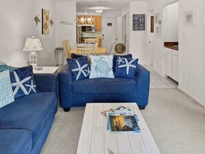 A living room with a blue sofa, a coffee table, and a dining area in the background.