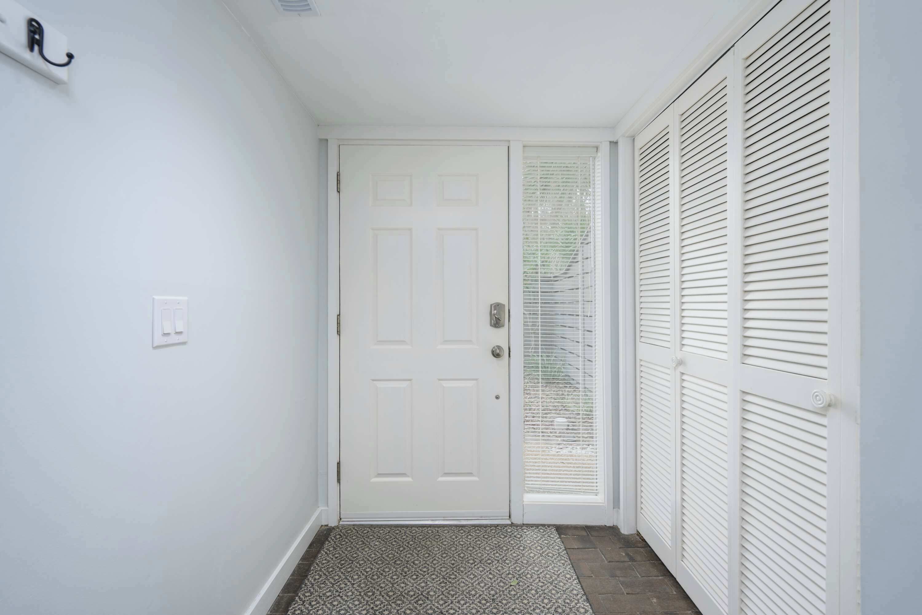 A hallway with a white door, a patterned rug, and a white closet with louvered doors.