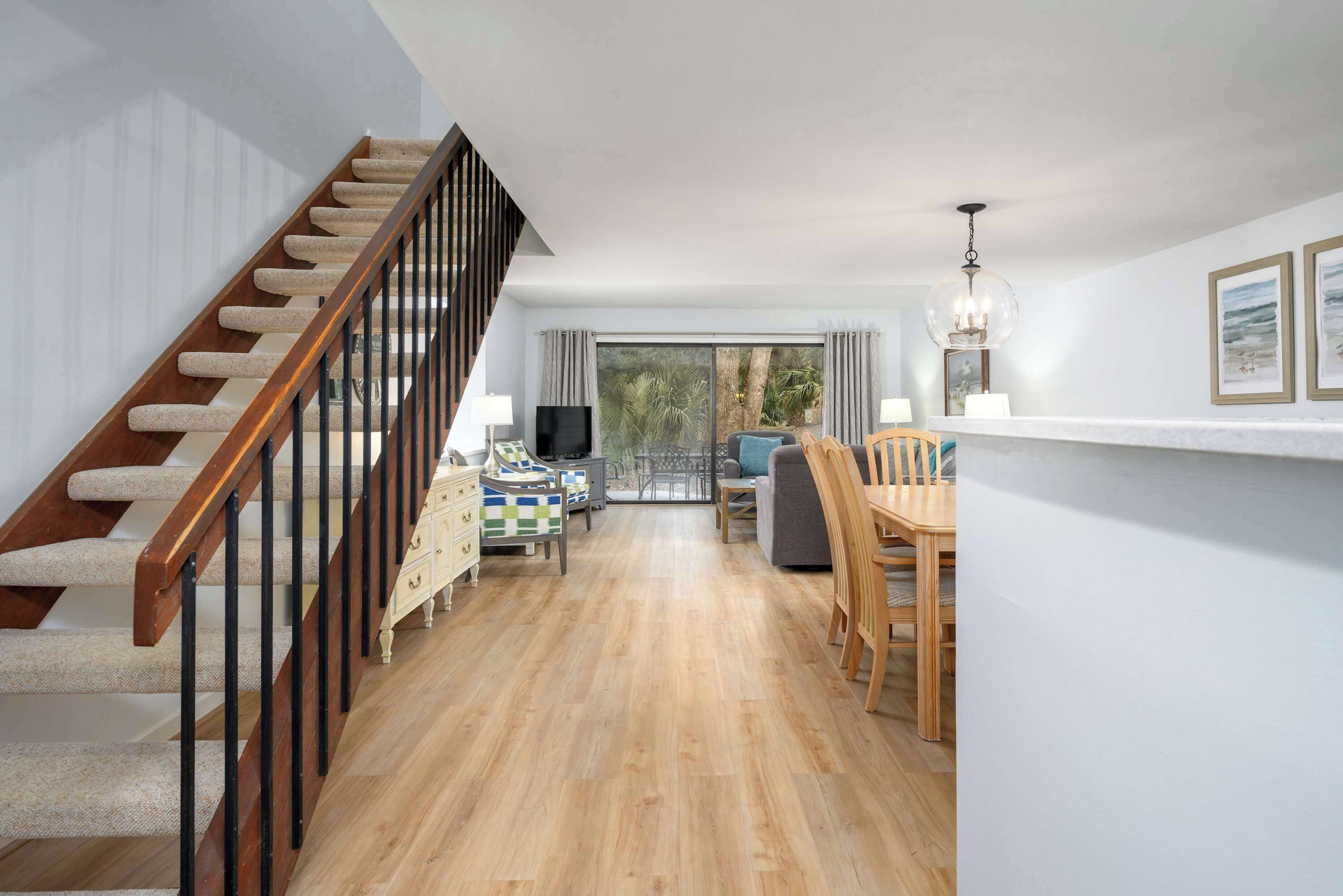 Een trap met houten treden en zwarte leuningen die leidt naar een woonruimte met een bank, eettafel en stoelen.