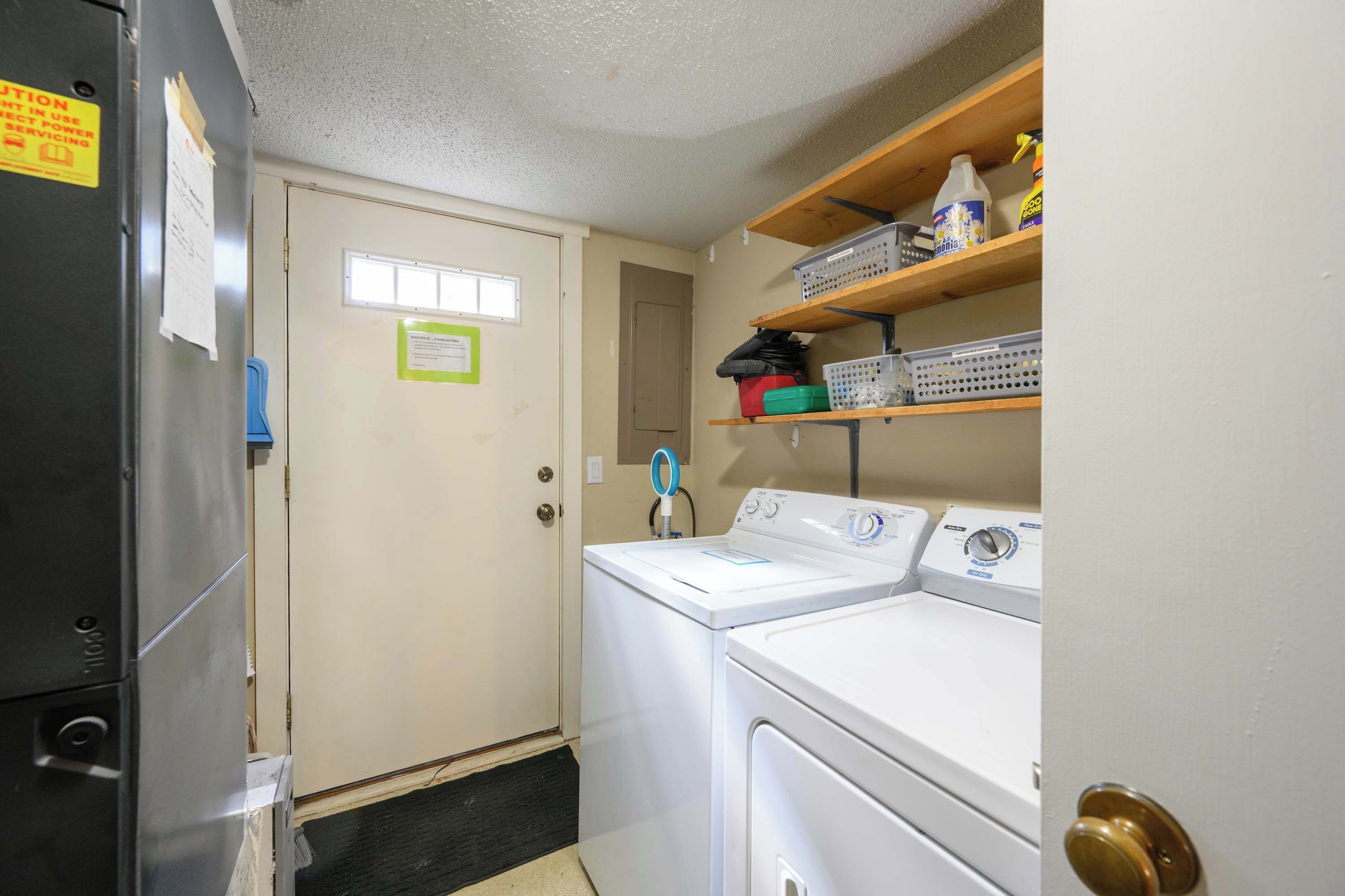 A laundry room with a washer and dryer, a door with a window, and shelves with cleaning supplies.