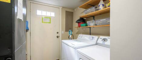 A laundry room with a washer and dryer, a door with a window, and shelves with cleaning supplies.