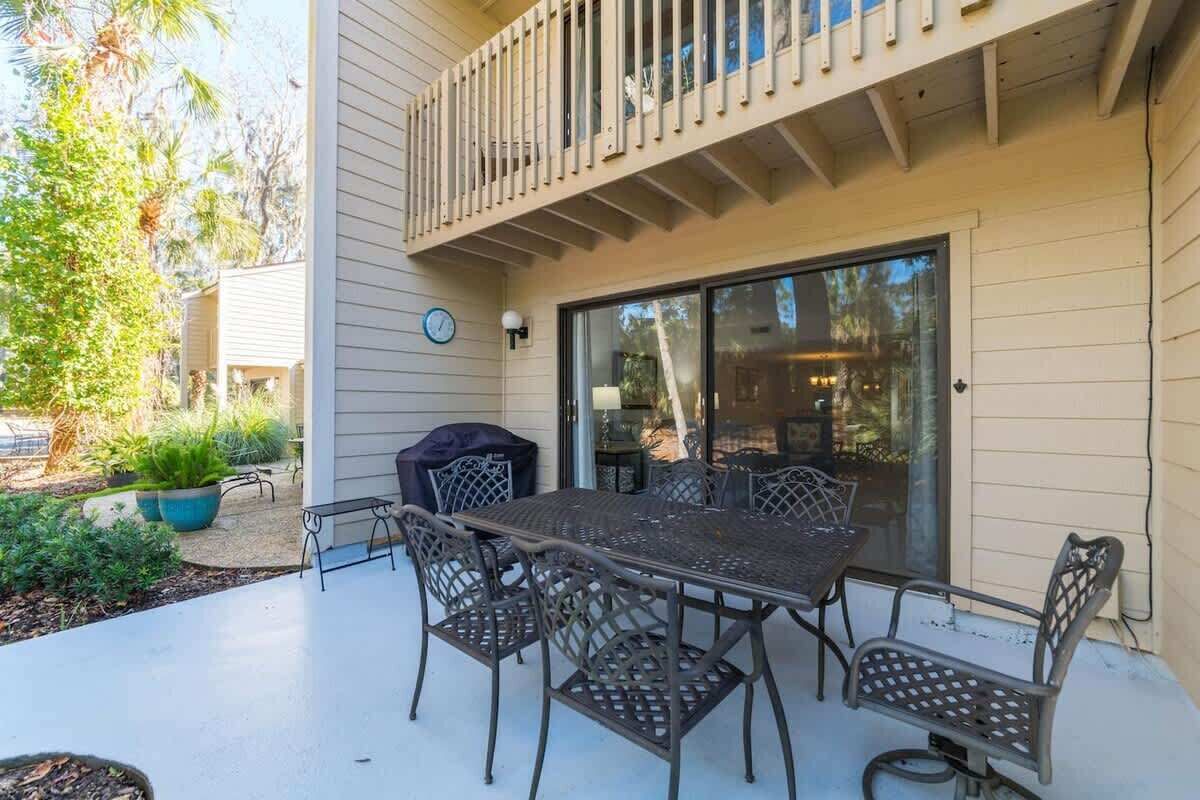 Een terras buiten met een metalen tafel en stoelen, een overdekte barbecue en een schuifdeur die leidt naar een overdekt terras.