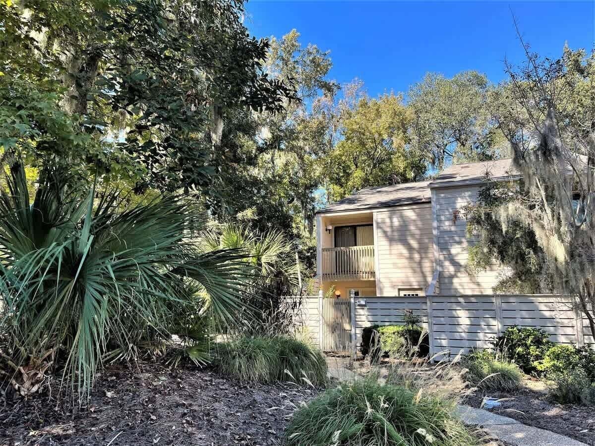 A two-story house with a balcony, surrounded by dense vegetation and trees.