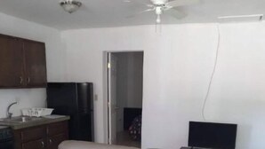 Un ambiente compatto con angolo cottura, divano, televisione e ventilatore a soffitto.