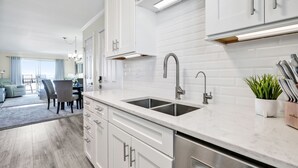 A modern kitchen with white cabinetry, stainless steel appliances, and a large island with a sink. - Amazing Ocean Views From Your Newly Renovated Oceanfront Condo in Carolina Beach (Carolina Beach)