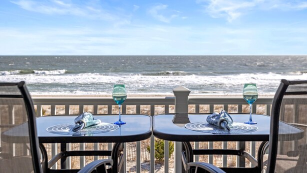 Two tables with chairs facing the ocean, each with a glass and a napkin. - Amazing Ocean Views From Your Newly Renovated Oceanfront Condo in Carolina Beach (Carolina Beach)