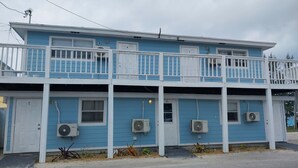 Un immeuble de deux étages doté d’un balcon, de portes numérotées et de climatiseurs.