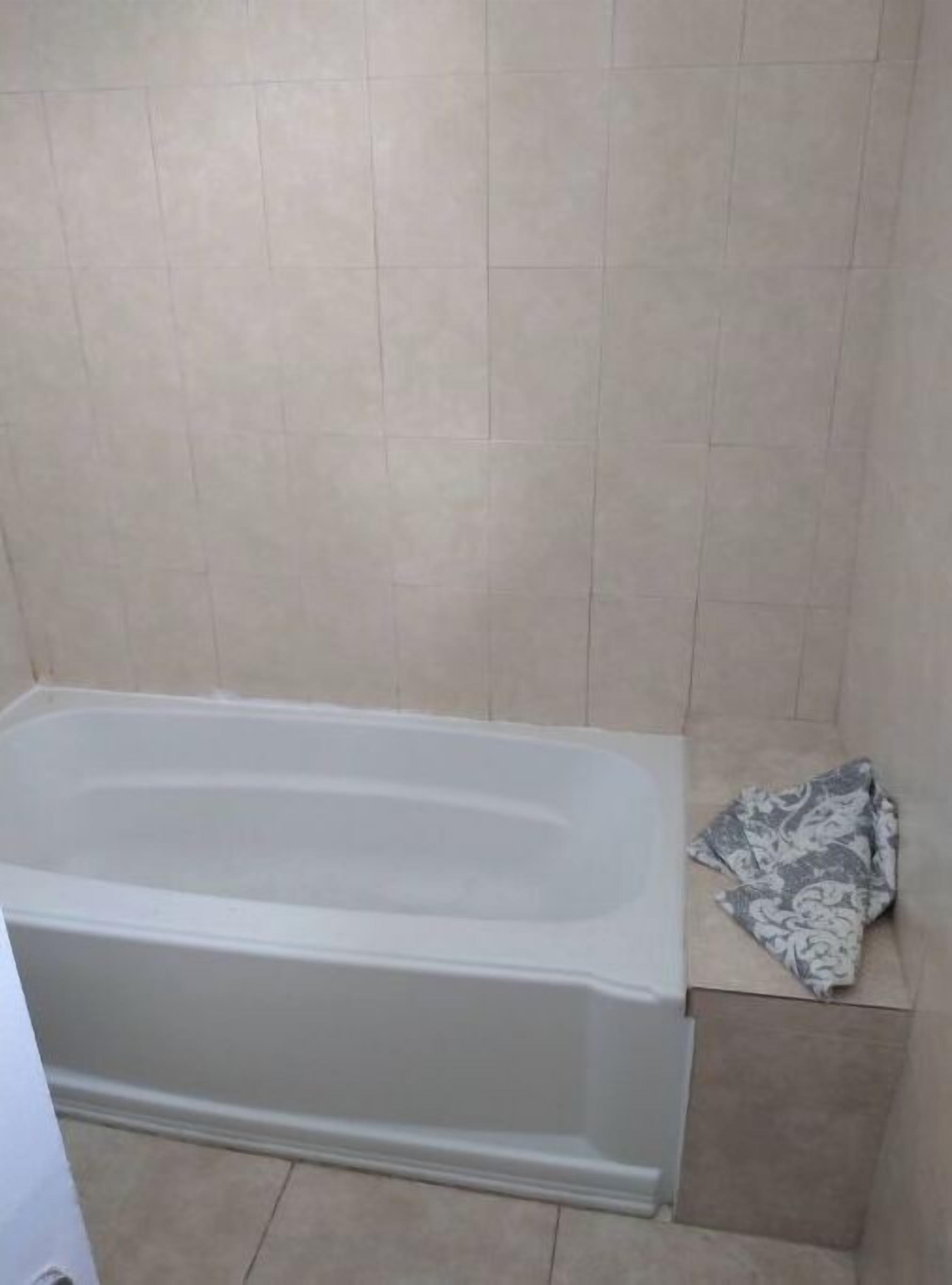 A bathroom with a bathtub, tiled walls, and a towel on a box.