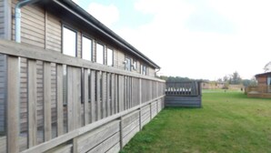 A wooden building with a fenced area and a grassy field. - Spacious 2-bed Lodge in Bury Saint Edmunds (Bury St Edmunds)