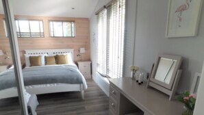A bedroom with a bed, bedside tables, a desk, and a window with blinds. - Spacious 2-bed Lodge in Bury Saint Edmunds (Bury St Edmunds)
