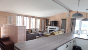 A modern kitchen with a wooden countertop, a built-in oven, and a sink. There is a dining area with a table and chairs, and a living room with a sofa and a television. - Spacious 2-bed Lodge in Bury Saint Edmunds (Bury St Edmunds)