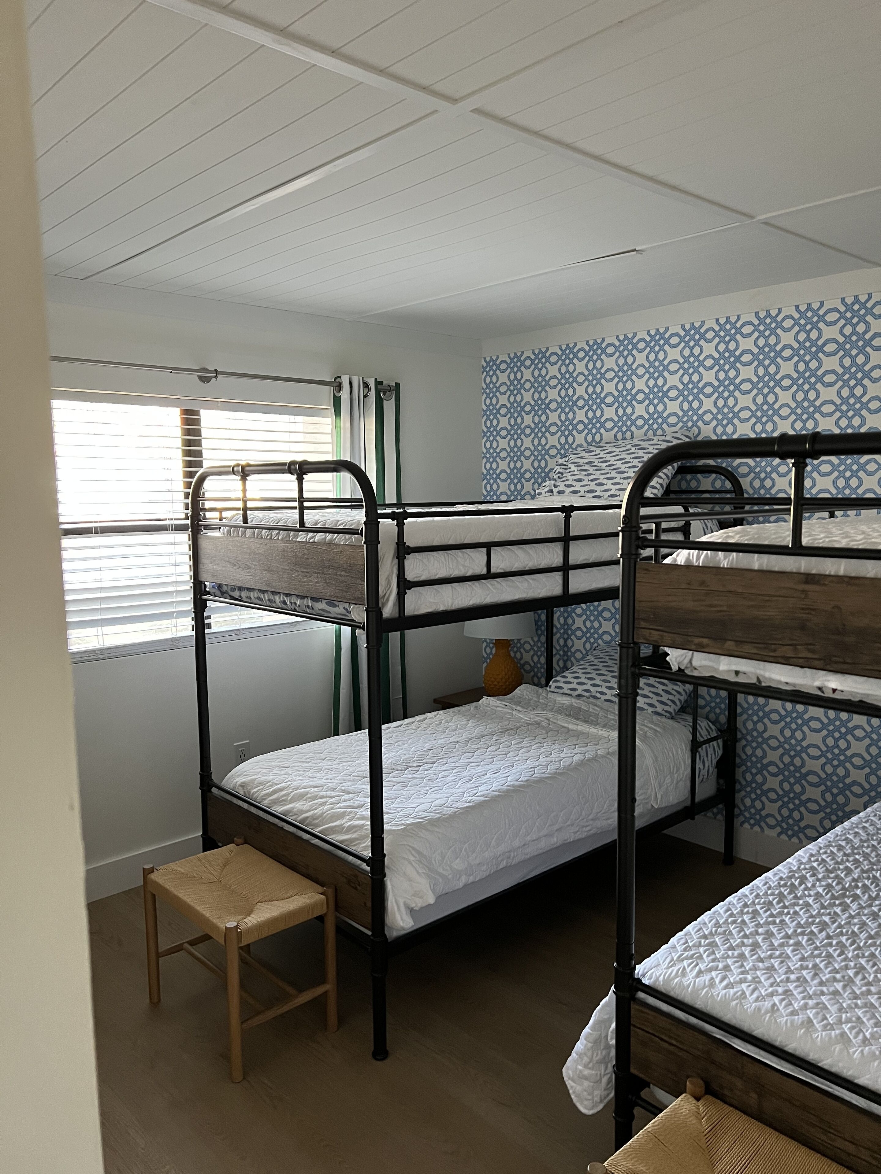 Un dormitorio con literas, un taburete pequeño de madera y papel tapiz estampado.