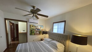 A hotel room with a bed, a ceiling fan, an air conditioning unit, a painting, a window, and a nightstand with a lamp. - Villa M - 1bedroom villa with kitchen, steps from downtown Palm Springs! 🍒 (Palm Springs)