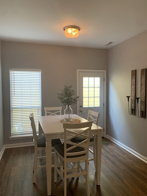 A dining room with a white table and chairs, a vase with a plant, and a door with a window.