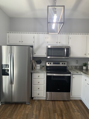 A modern kitchen with stainless steel appliances, white cabinetry, and a wooden floor.