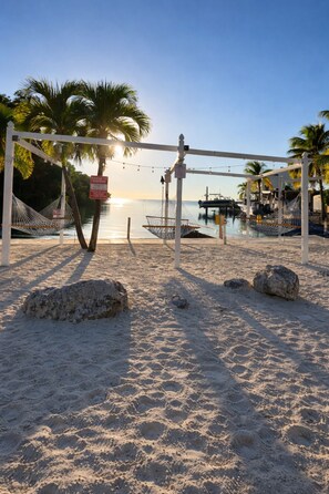 A beach volleyball court with a net, palm trees, and a sunset in the background. - Calusa Campground #50- RV in Key Largo Florida Keys Vacation Paradise Place (Key Largo)