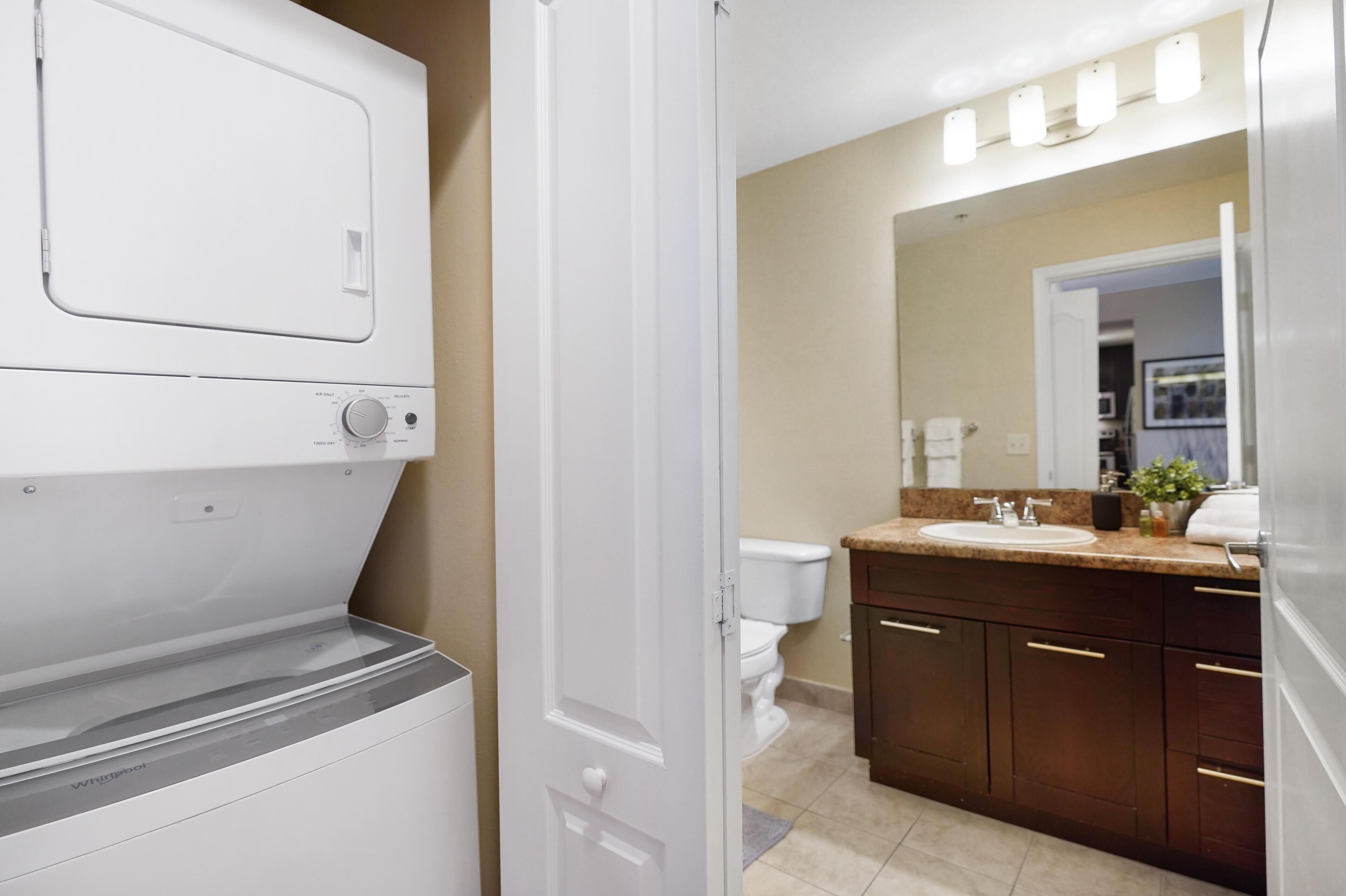 A modern bathroom with a built-in washer and dryer, a large mirror, a sink, and dark wooden cabinets.