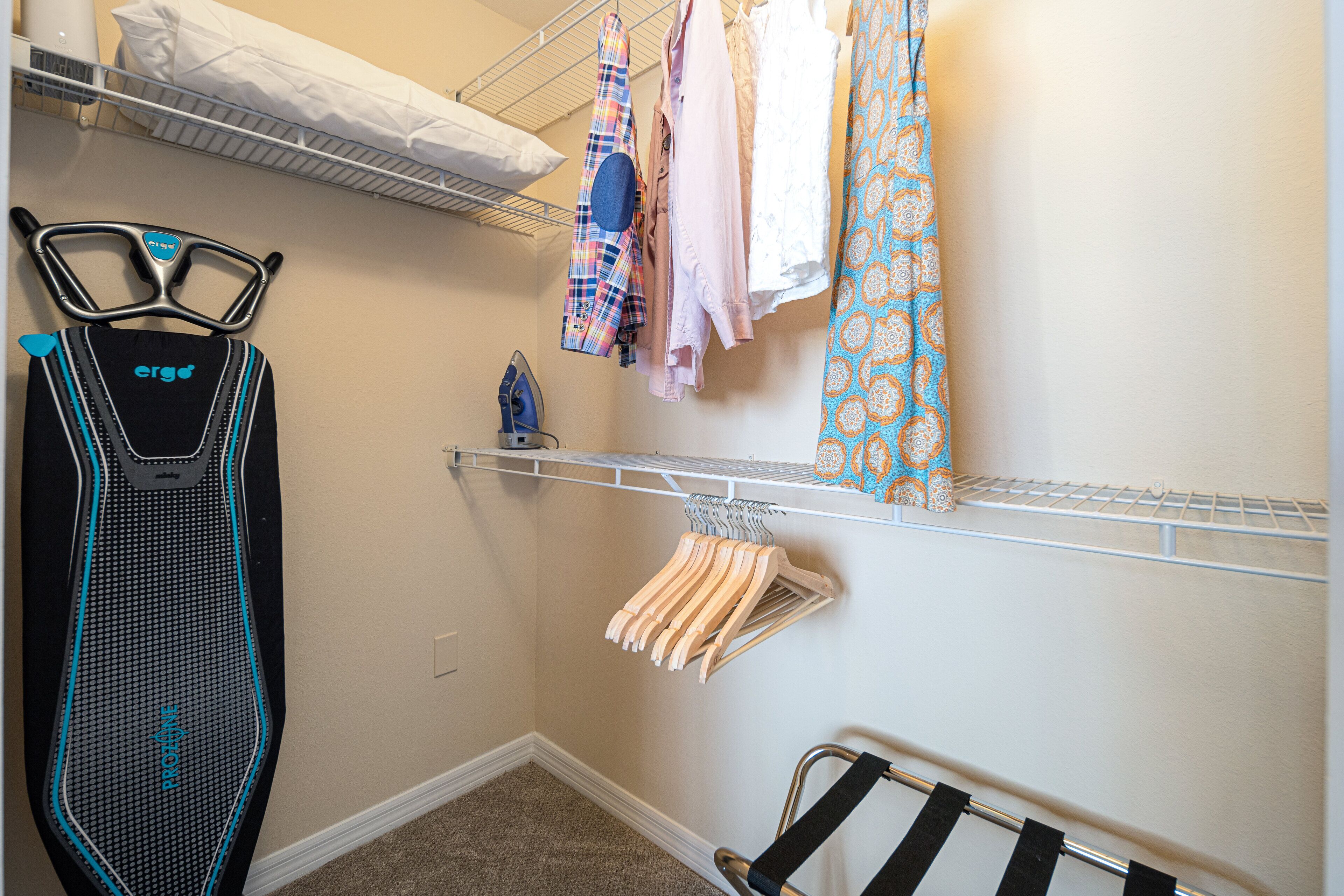 A laundry area with a drying rack, ironing board, and hanging clothes.