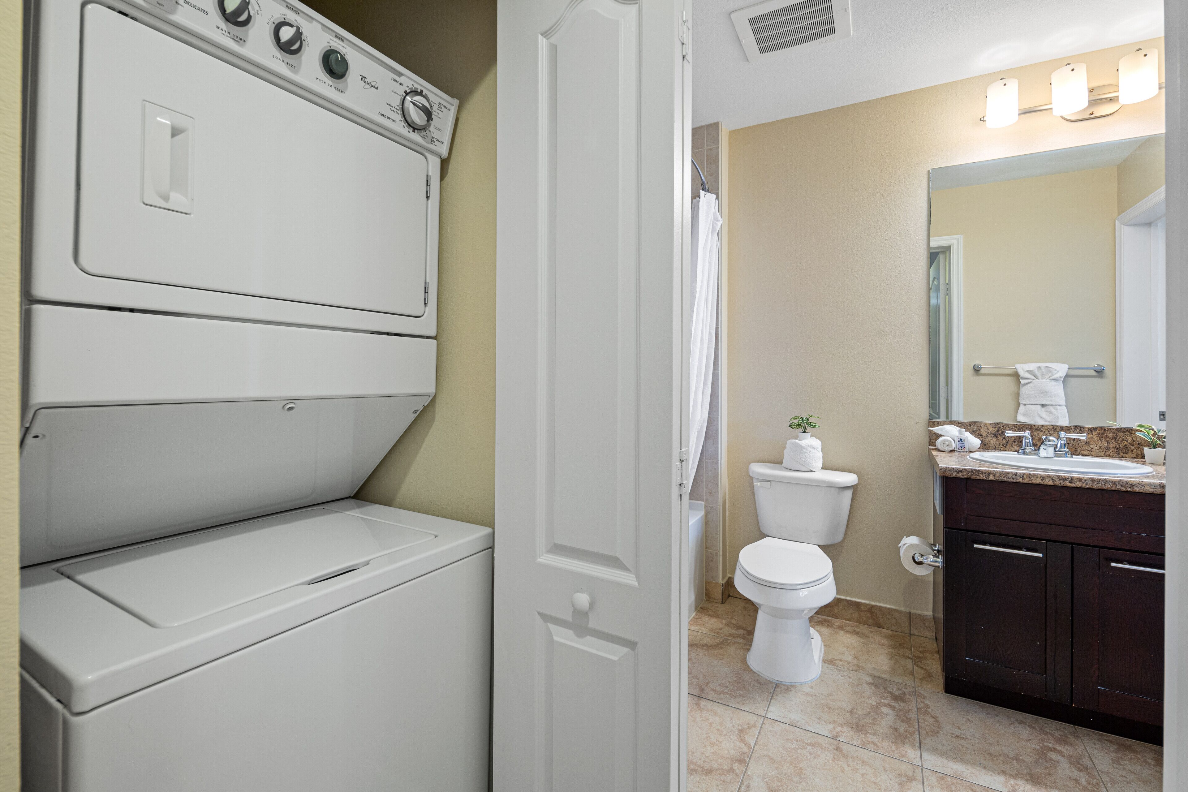 A laundry room with stacked washers and dryers, a toilet, and a sink with a mirror above it.