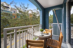 A balcony with a round table, two wooden chairs, a small potted plant, and a plate of croissants. - Dharma Home Suites South Miami at Red Road Commons (Miami)