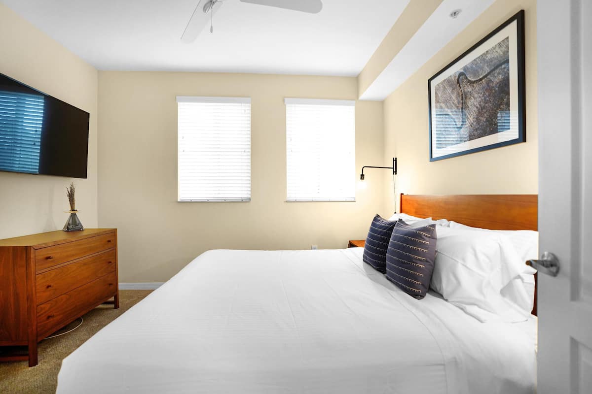 A bedroom with a large bed, a wooden dresser, a ceiling fan, and a framed picture on the wall.
