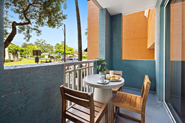 A balcony with a round table, two wooden chairs, a potted plant, and a view of a green park and buildings. - Dharma Home Suites South Miami at Red Road Commons (Miami)