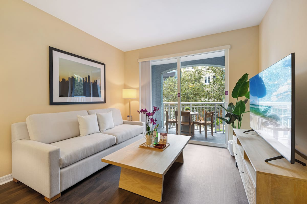 A modern living room with a sofa, coffee table, TV, and a balcony with plants.