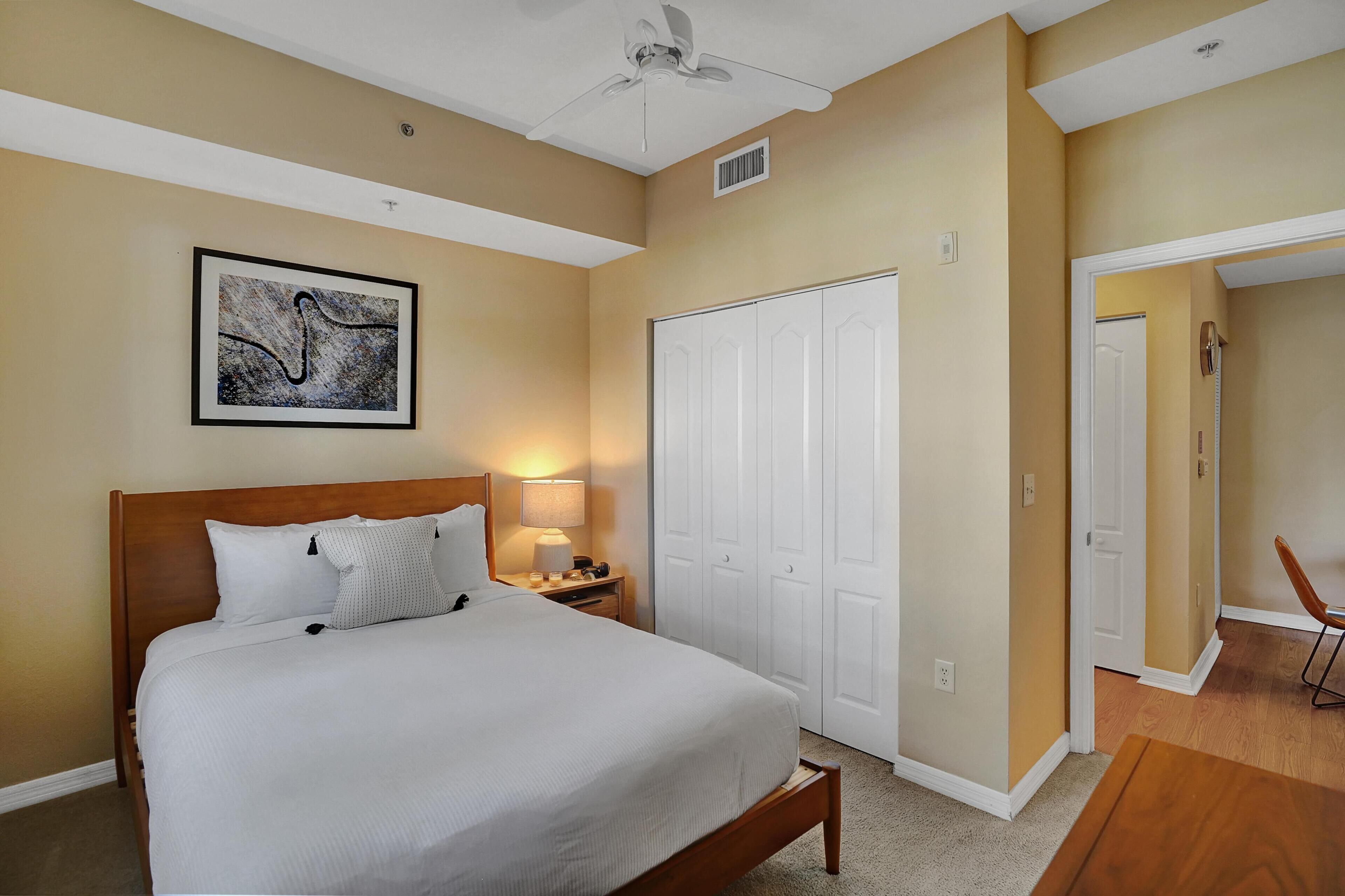 A neatly arranged bedroom with a large bed, a bedside table with a lamp, a framed artwork on the wall, and a wardrobe.