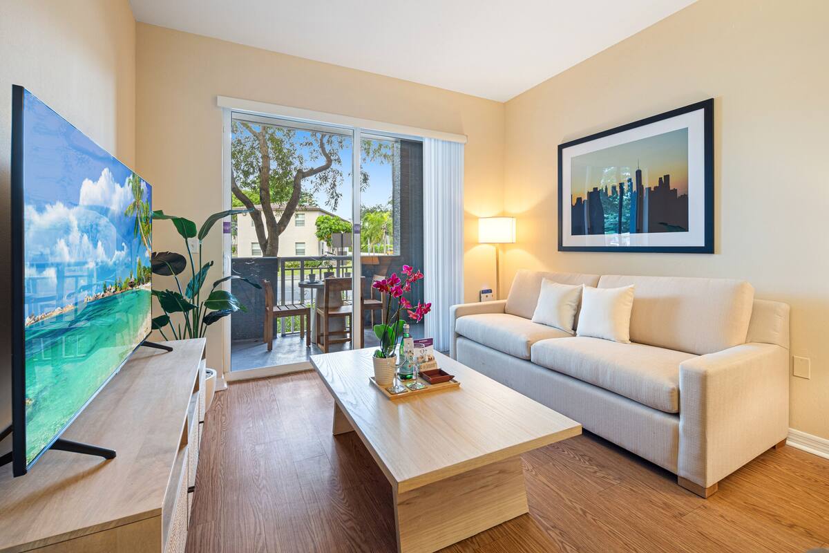 A modern living room with a large TV, a sofa, a coffee table, and a cityscape painting.