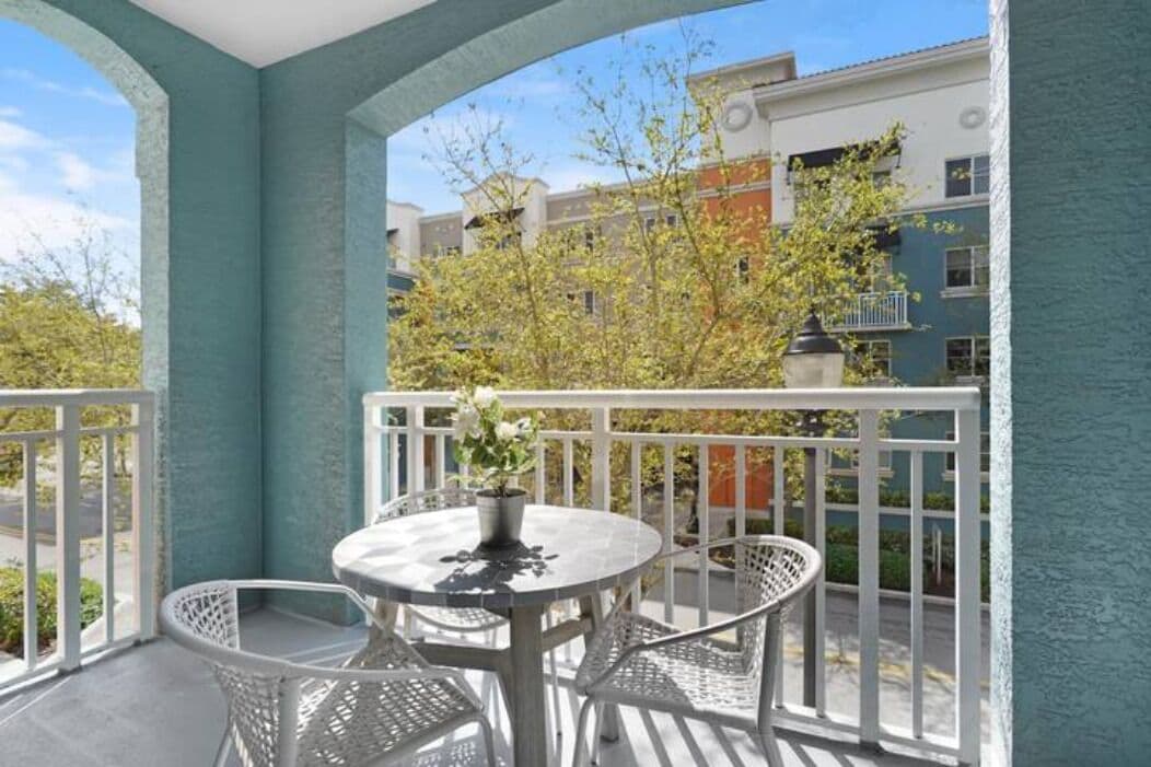 Ein Balkon mit rundem Tisch und Stühlen, einem Blumentopf und Blick auf Gebäude und Bäume.