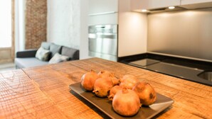 A kitchen with a wooden table displaying pomegranates, a modern stove, and a refrigerator. - SPECTACULAR GRAN VIA CHUECA EXTERIOR (Madrid)