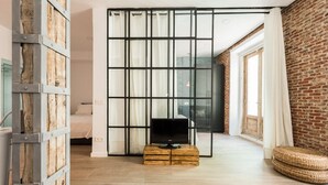 A modern living room with a television on a wooden crate, a large sliding glass door, and a brick wall. - SPECTACULAR GRAN VIA CHUECA EXTERIOR (Madrid)