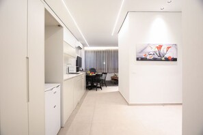 A modern kitchen with white cabinetry, a dining area with a table and chairs, and a living space with a large window and curtains.