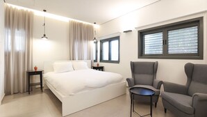 Une chambre à coucher moderne, avec un lit, deux tables de chevet, une chaise, une petite table et une fenêtre avec des stores.