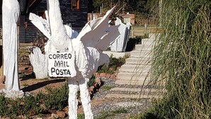Une boîte aux lettres sur laquelle on peut lire « CORREO MAIL POSTA », située dans un cadre rural, avec une maison en bois en arrière-plan.