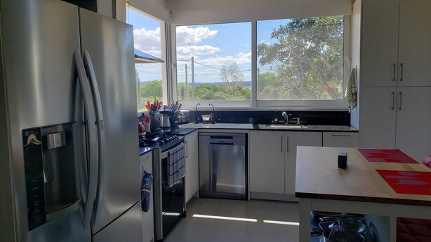 Une cuisine moderne dotée d’appareils électroménagers en acier inoxydable, d’une grande fenêtre offrant une vue sur la verdure et d’un aménagement intérieur compact.