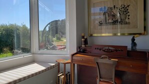 Une pièce avec une grande fenêtre, un bureau, une chaise et une bibliothèque.