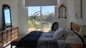 Une chambre à coucher comprenant un lit, une commode, un miroir et donnant sur une structure circulaire située à l’extérieur.
