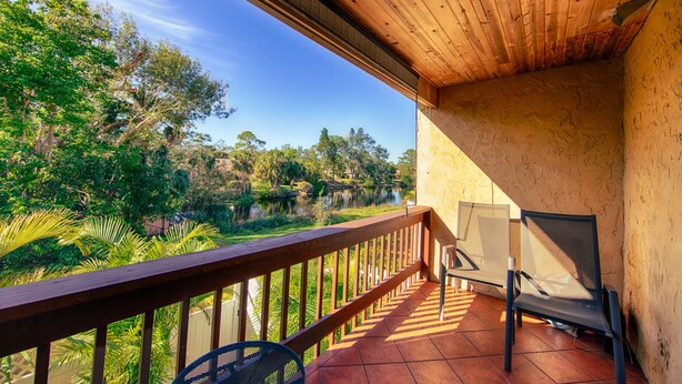 A balcony with a wooden railing, a chair, and a view of a lake surrounded by trees. - Lake view spacious 2bdr CONDO 7 min by the BEACH (Sarasota)