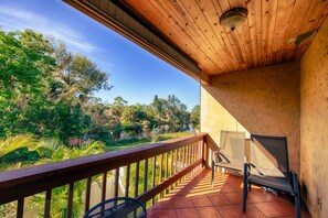 A balcony with a wooden railing, a chair, and a view of a lake surrounded by trees.