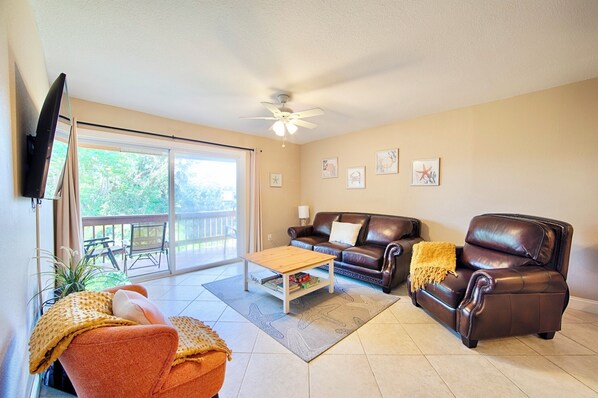 A living room with a brown leather sofa, a wooden coffee table, and a TV mounted on the wall.