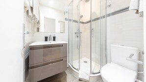 Une salle de bain moderne avec une douche à parois de verre, des toilettes blanches et un meuble-lavabo avec un miroir.