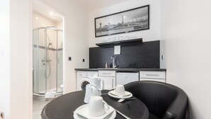 Une cuisine moderne avec un coin repas, comprenant une table ronde avec de l’assiette et des tasses blanches, une chaise noire et une cabine de douche en verre.