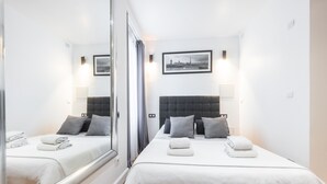 Une chambre d’hôtel avec deux lits, un grand miroir, un tableau représentant un paysage urbain accroché au mur, et un lit soigneusement fait avec des serviettes.