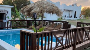 A wooden deck with lounge chairs and a thatched umbrella, overlooking a swimming pool. - Private 2 bedroom Casitas with pool. Azteca villas (Treasure Beach)