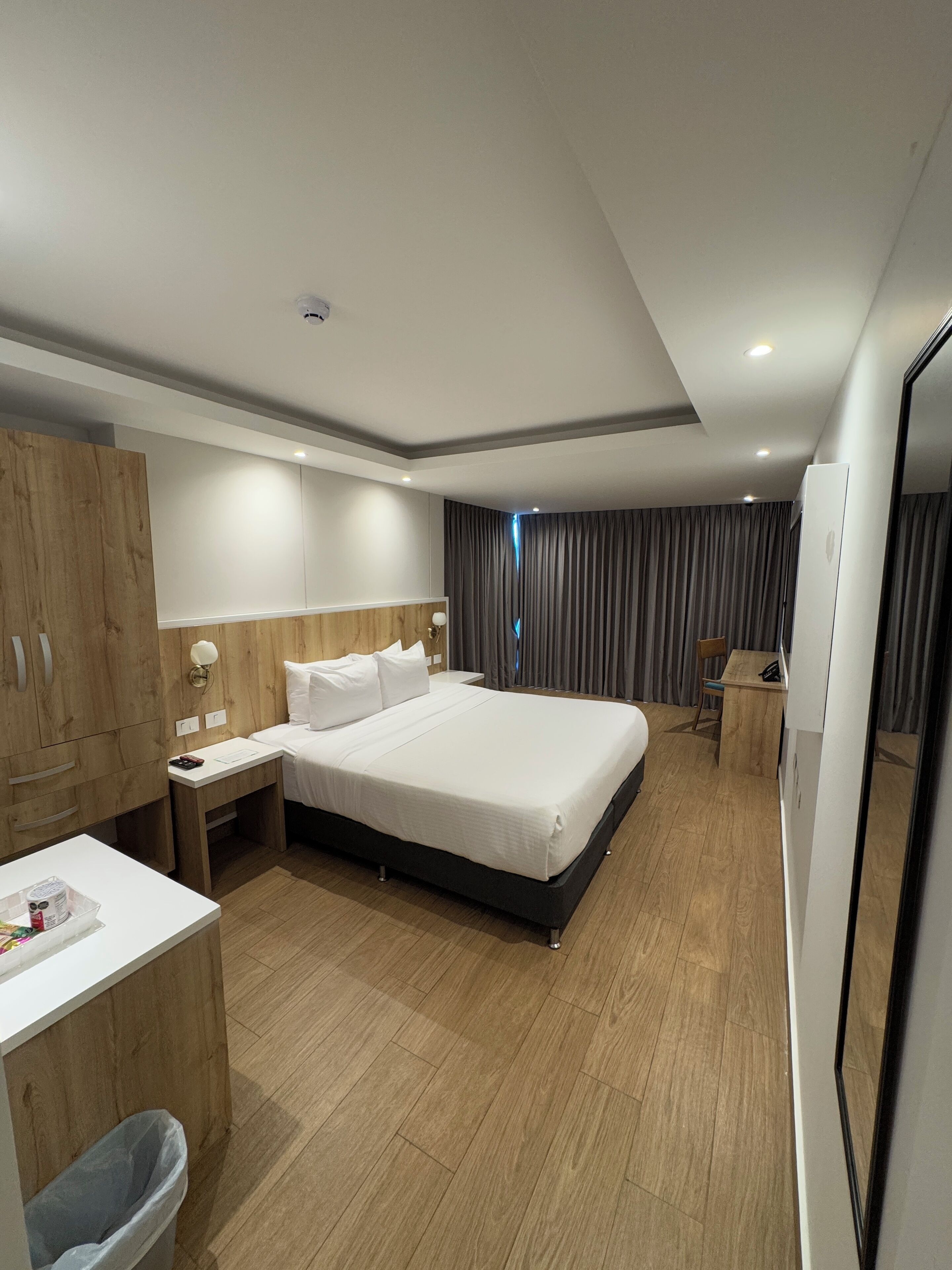 Una habitación de hotel moderna con una cama grande, un armario de madera, una mesita de noche y una pequeña zona de escritorio.